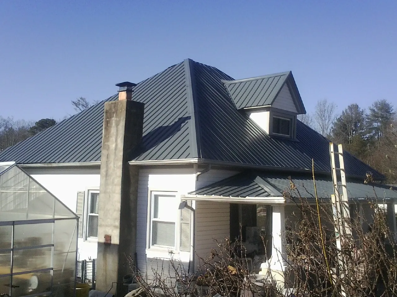 Dark blue standing seam metal roof on a white farmhouse with dormer — Slate & Tile Roof Repair by Roofing Brothers in Lockhart