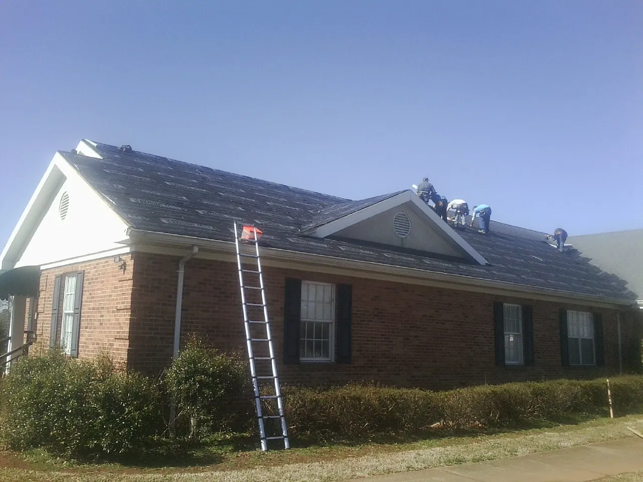 Crew tearing shingles off a brick ranch roof with a ladder set — Metal Roof Repair work by our crew in Lockhart