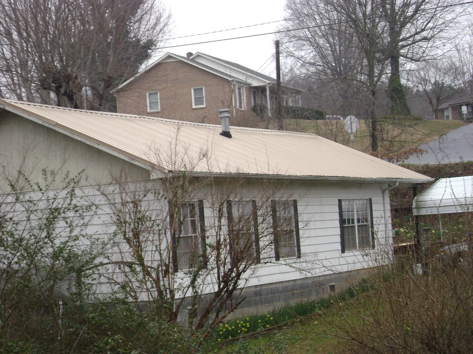 Tan metal roof on a white sided house set into a hillside — Commercial Roofing by Roofing Brothers in Lockhart